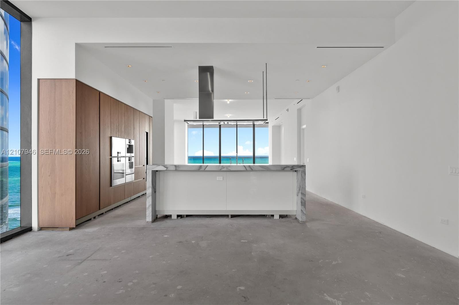 Contemporary kitchen featuring full-height wood cabinetry, a waterfall-edge stone island, built-in stainless steel appliances, a ceiling-mounted range hood, and floor-to-ceiling windows