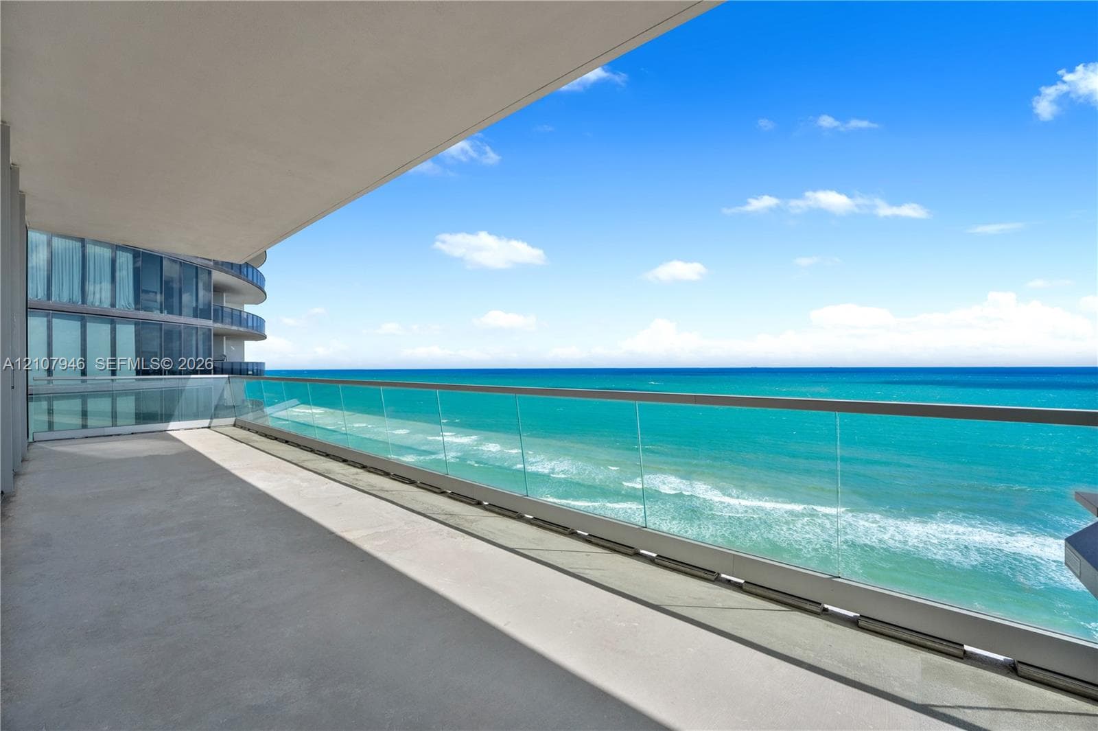 Expansive balcony featuring a glass-panel railing, concrete flooring, and a deep overhead overhang