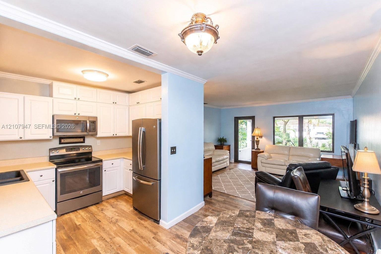 Kitchen featuring white cabinetry, stainless steel appliances, and wood-finish flooring, complemented by a semi-open floor plan with crown molding
