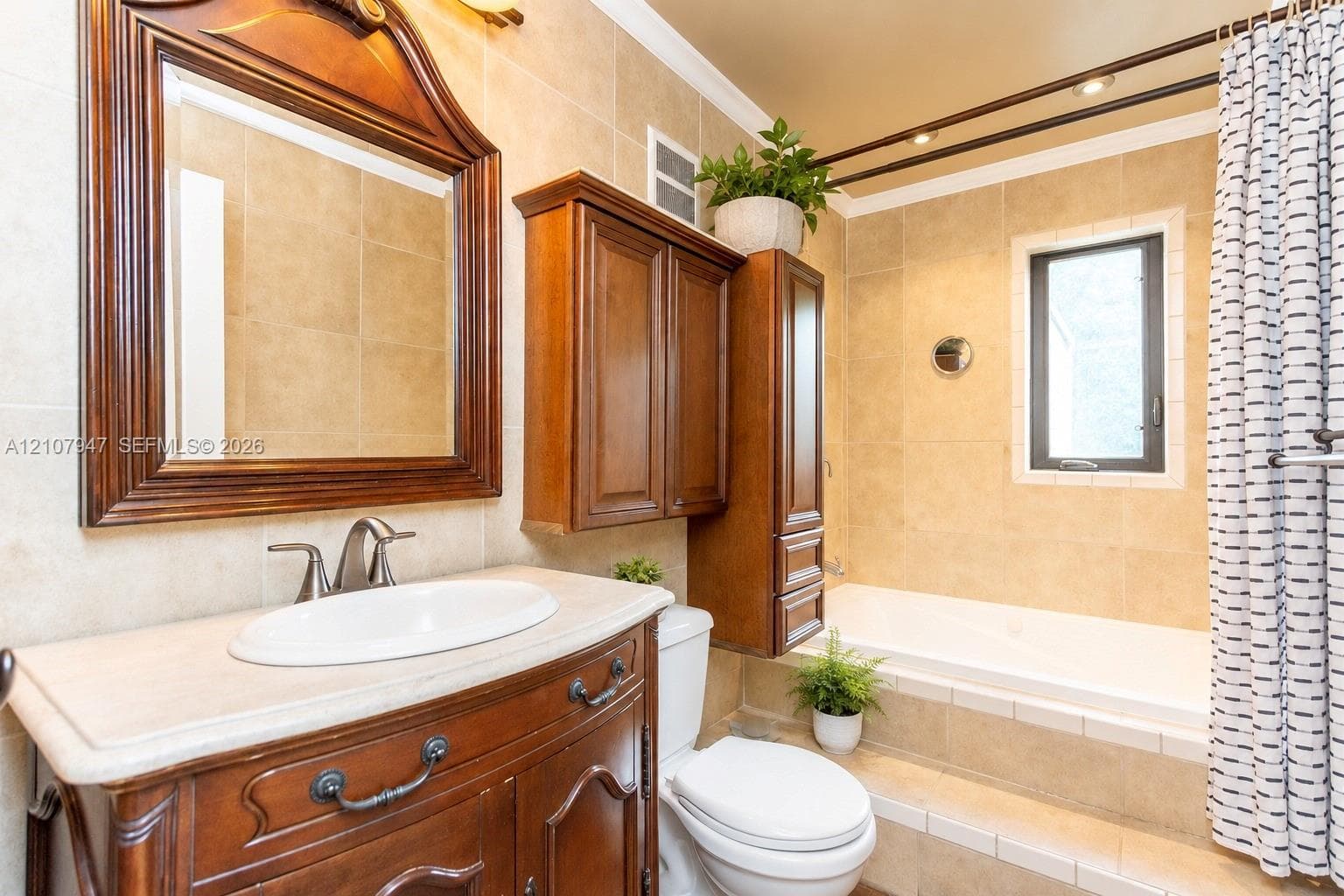 Bathroom featuring a wood vanity with an integrated oval sink and stone-finish countertop, matching wood-frame wall mirror, wall-mounted wood cabinetry, built-in soaking tub with a tile surround, and neutral wall tile throughout