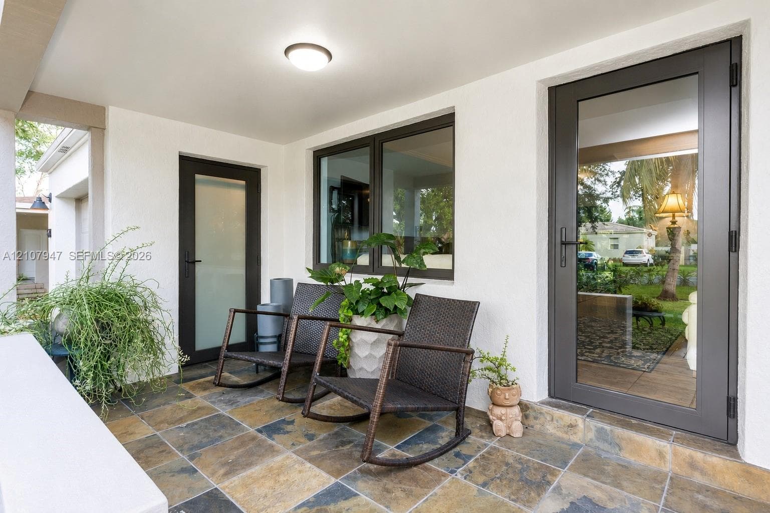 Covered porch featuring multi-tonal slate tile flooring, two full-light glass doors with matte black hardware, and a dual-pane window