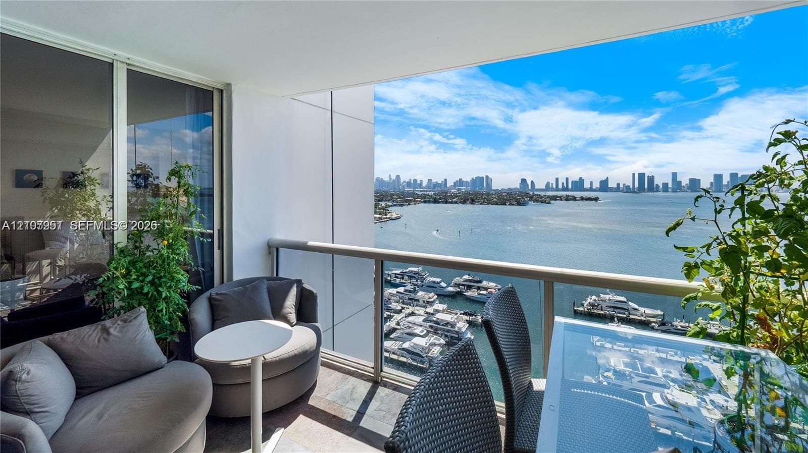 Covered balcony featuring tile flooring and a glass-paneled railing overlooking the waterfront and cityscape