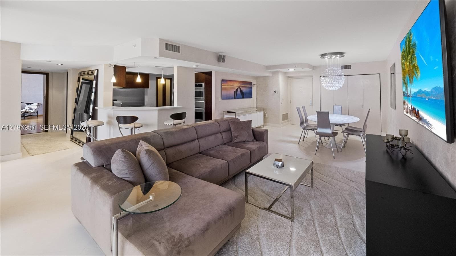 Open-concept living space featuring neutral tile flooring, breakfast bar with pendant lighting, built-in double wall oven, and a modern sphere-style chandelier