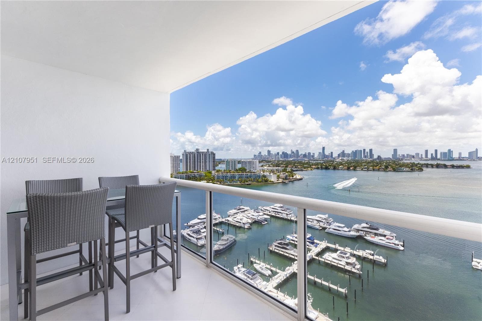 Covered balcony featuring tile flooring and a glass-paneled railing overlooking the harbor and urban skyline