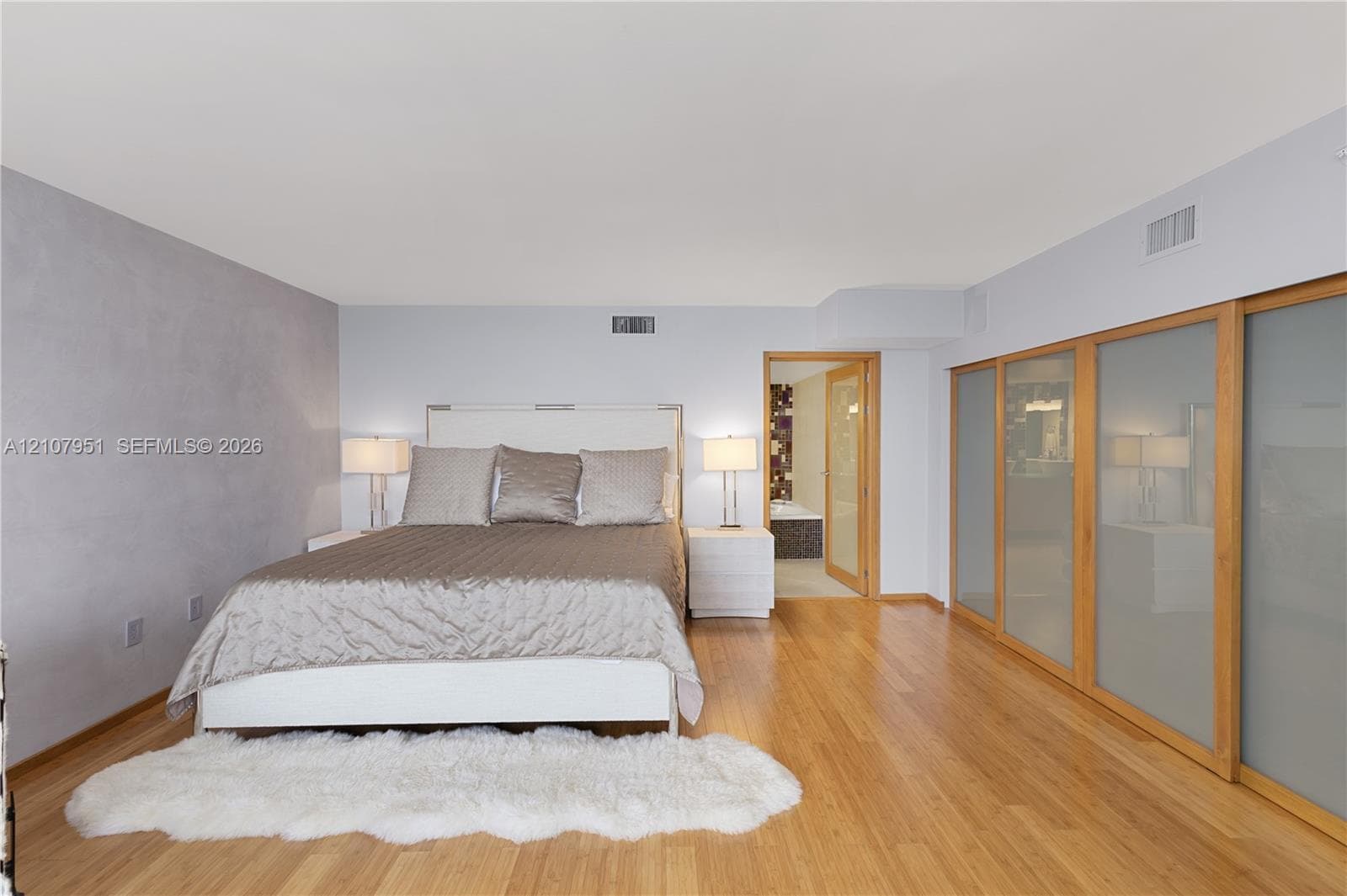 Wood-finish flooring, textured accent wall, and floor-to-ceiling sliding closet doors with frosted glass panels