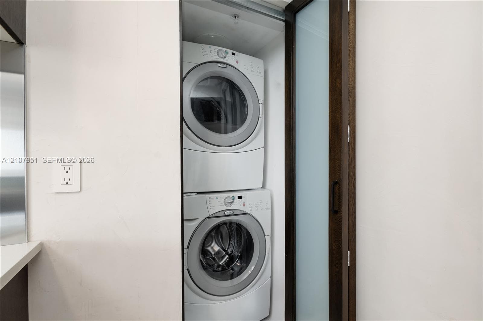 Stacked laundry unit featuring front-loading machines enclosed by a frosted glass door with a dark wood-finish frame