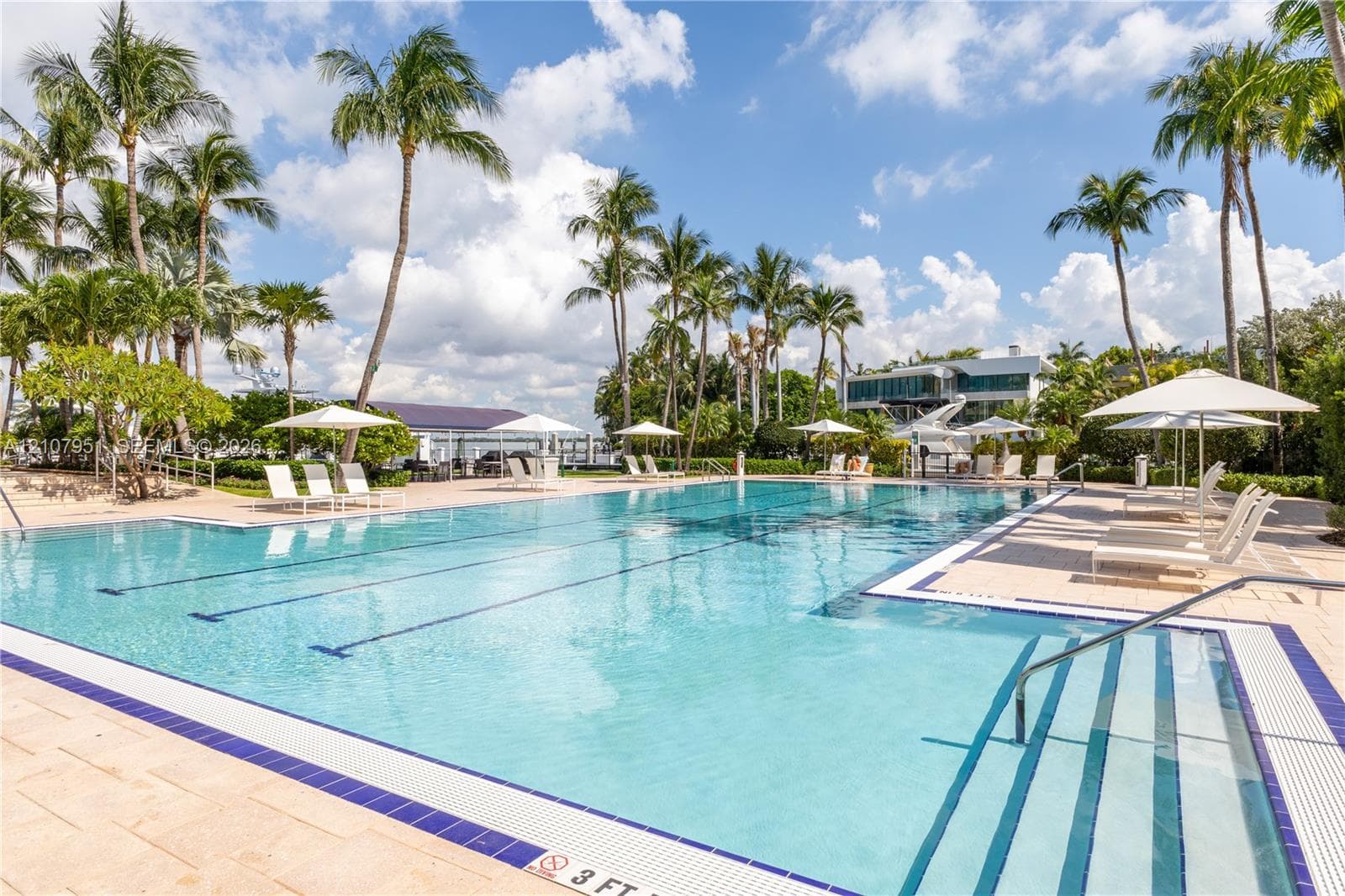 Full-length lap pool featuring blue tile accents, multi-level stairs with metal handrails, and surrounding stone paver deck