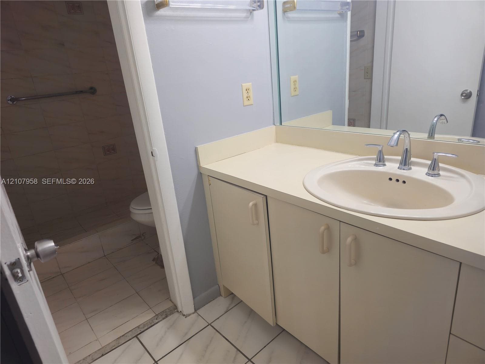 Bathroom featuring a vanity with integrated sink and chrome faucet, large vanity mirror, tile flooring, and a separate enclosed area with tile-surround shower