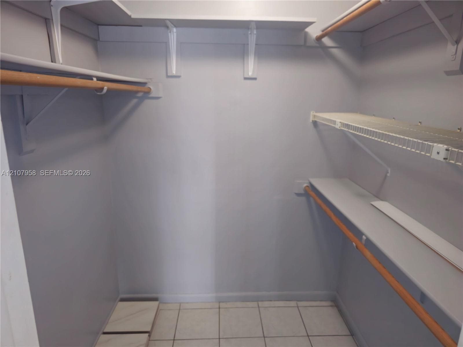 Walk-in closet featuring multi-level shelving, wood-finish clothing rods, and tile flooring