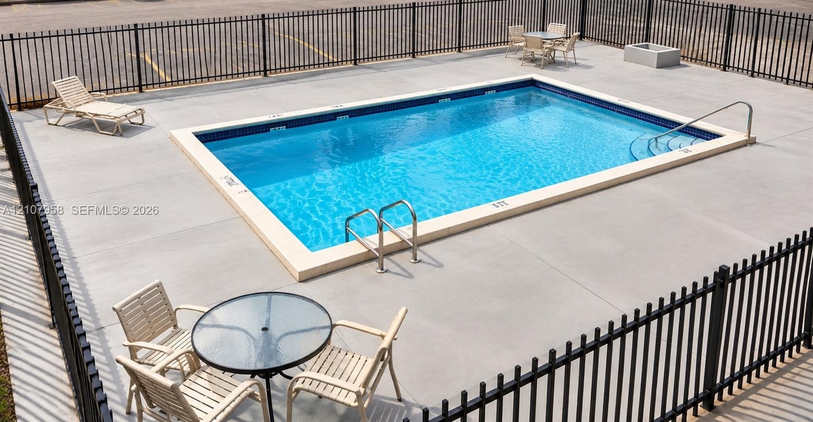 In-ground swimming pool featuring a concrete deck, tiled waterline, integrated metal handrails, and a perimeter metal fence