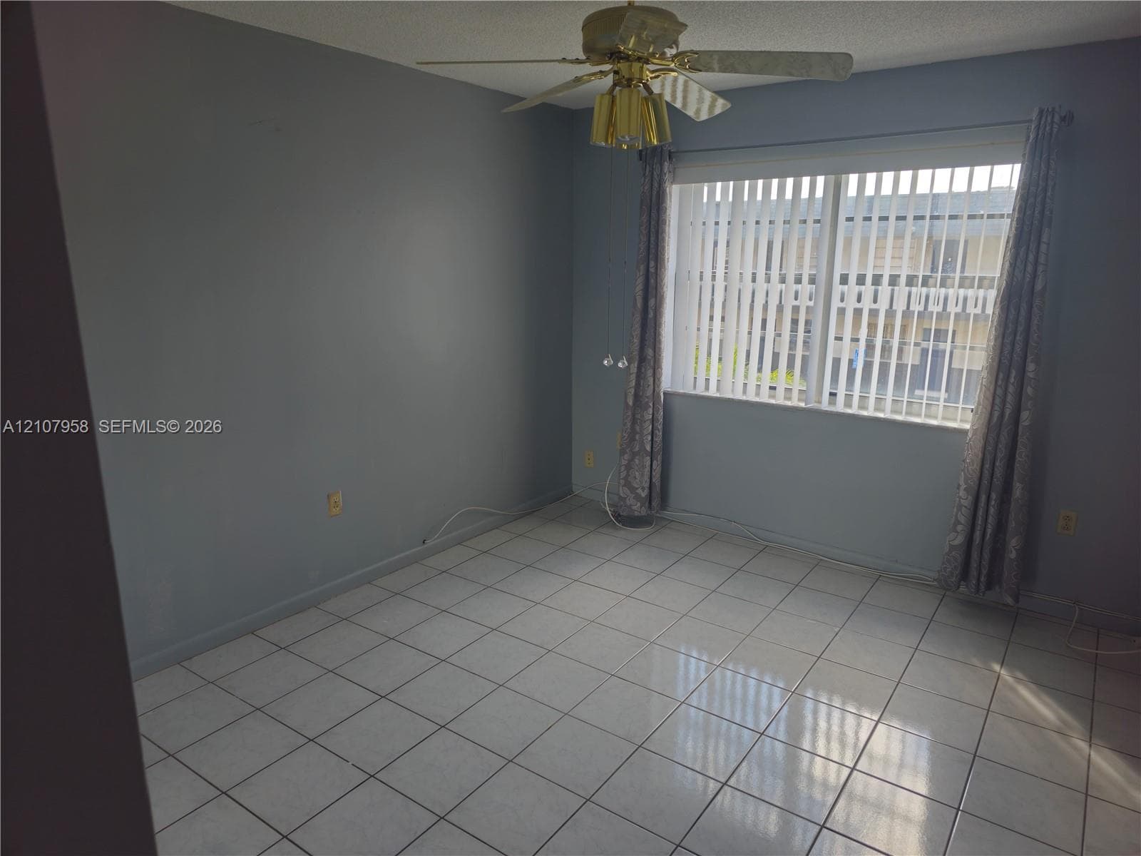 Room interior featuring ceramic tile flooring, a multi-blade ceiling fan with integrated lighting, and a large window with vertical blinds