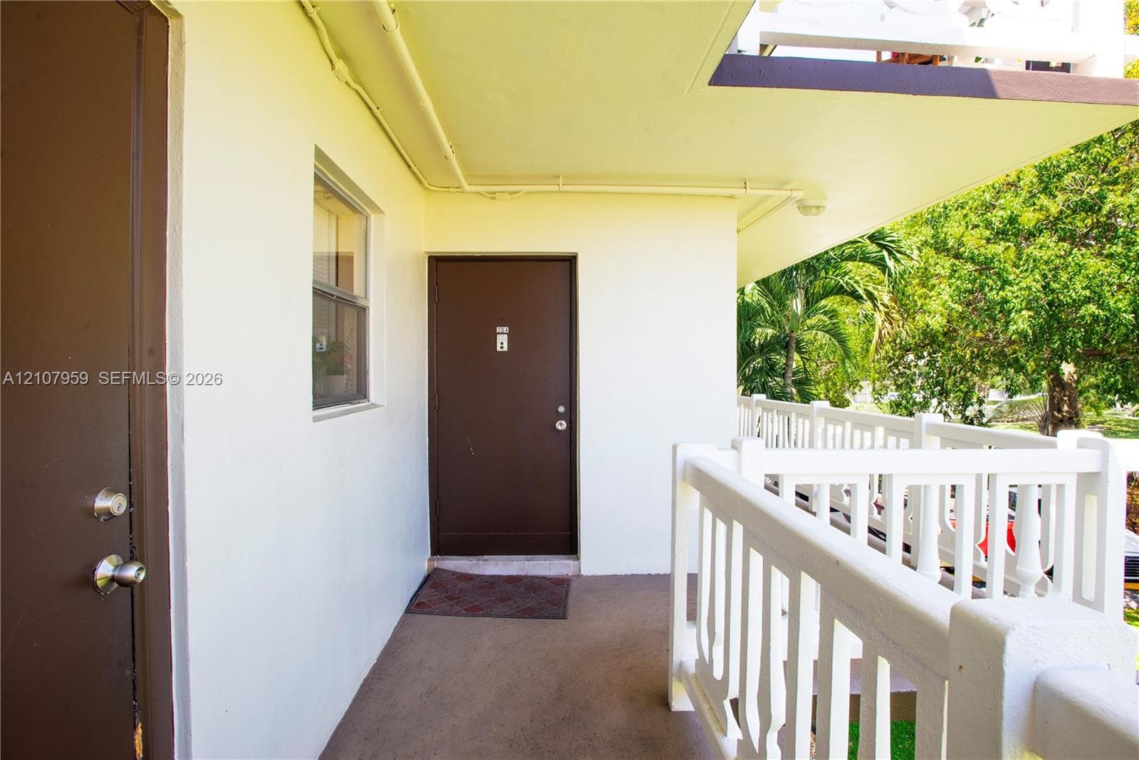 Covered exterior walkway featuring a concrete floor, solid-core doors with metallic hardware, and a white balustrade railing