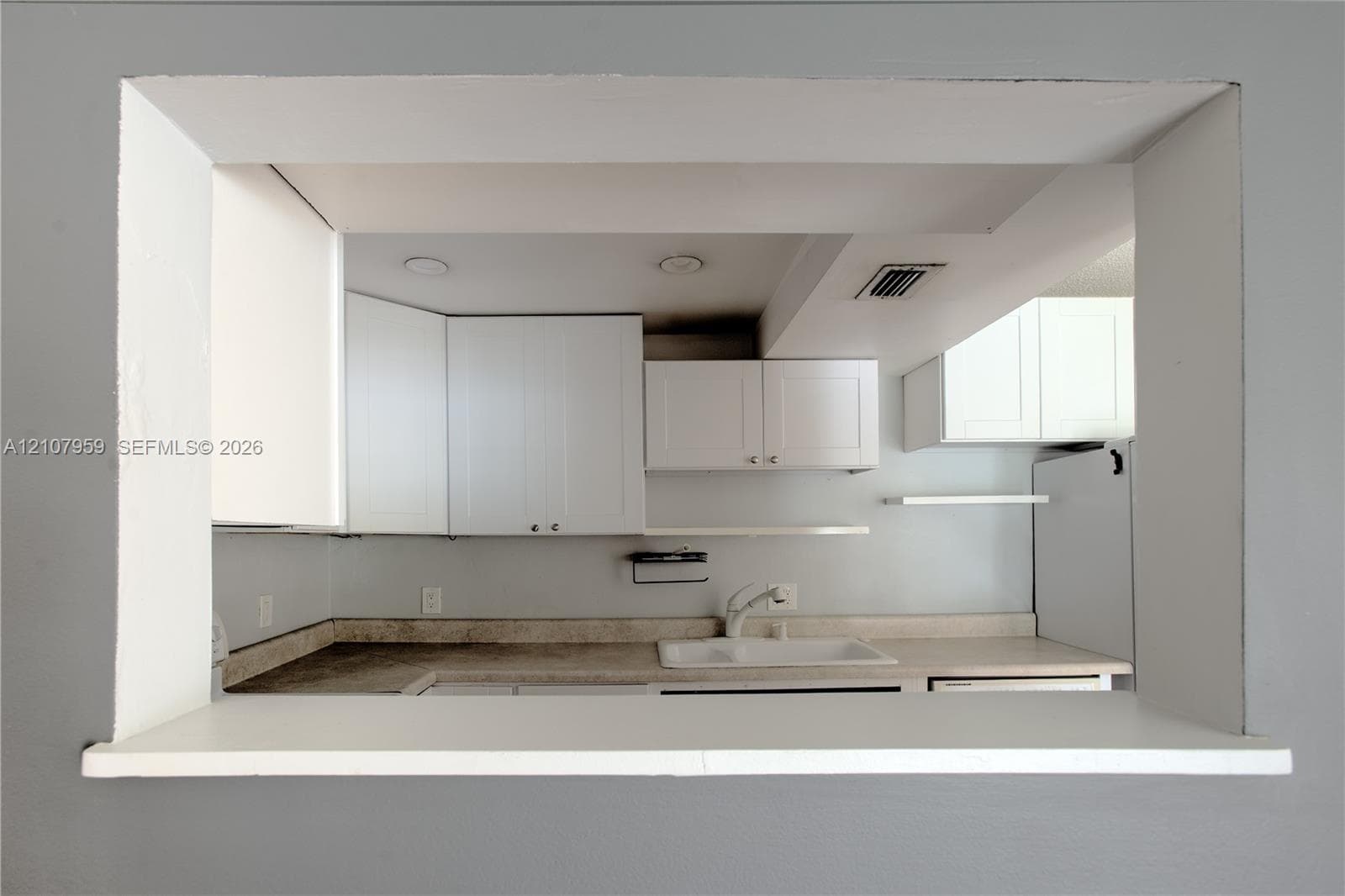 Pass-through opening featuring white cabinetry, solid-surface countertops, recessed lighting, and a white sink