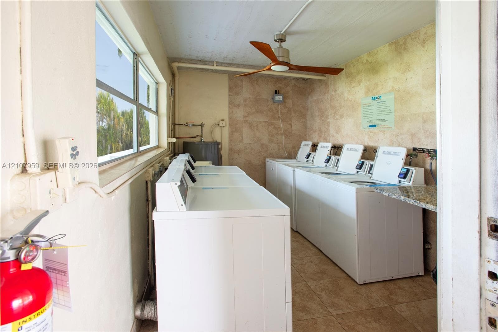 Utility space featuring stone tile wall cladding and flooring, a ceiling fan, and multiple top-load washer and dryer units with stone countertop surfacing