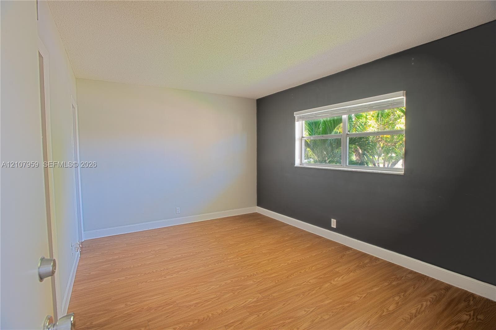 Room featuring wood-finish flooring, a dark charcoal accent wall, neutral painted walls, and a horizontal window with a fitted roller shade