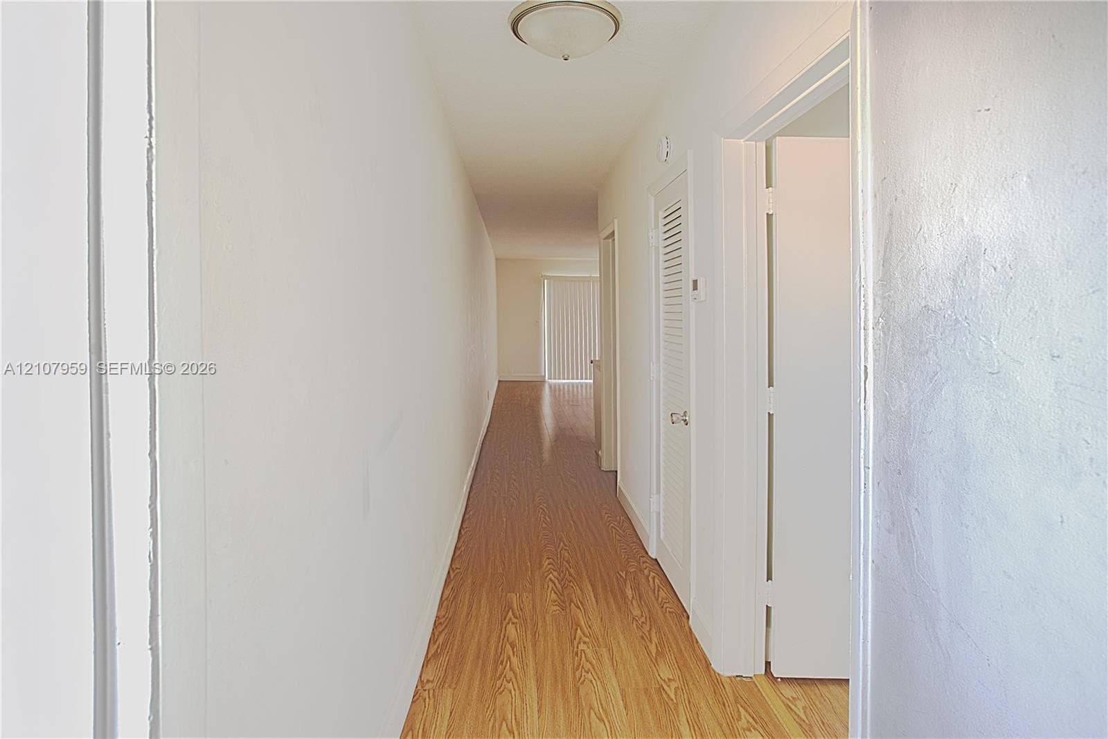 Hallway featuring wood-finish flooring, flush-mount ceiling lighting, and louvered closet doors