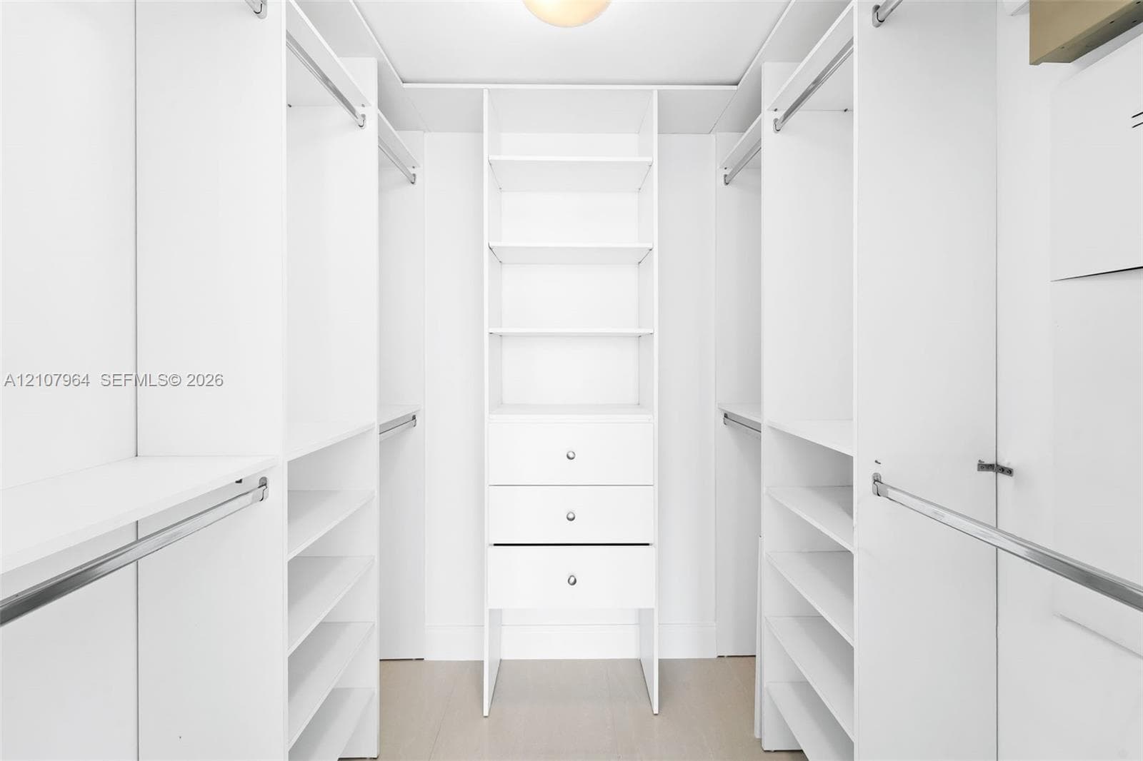 Custom walk-in closet featuring white built-in shelving, triple stacked drawers with hardware, multiple hanging rods, and wood-finish flooring
