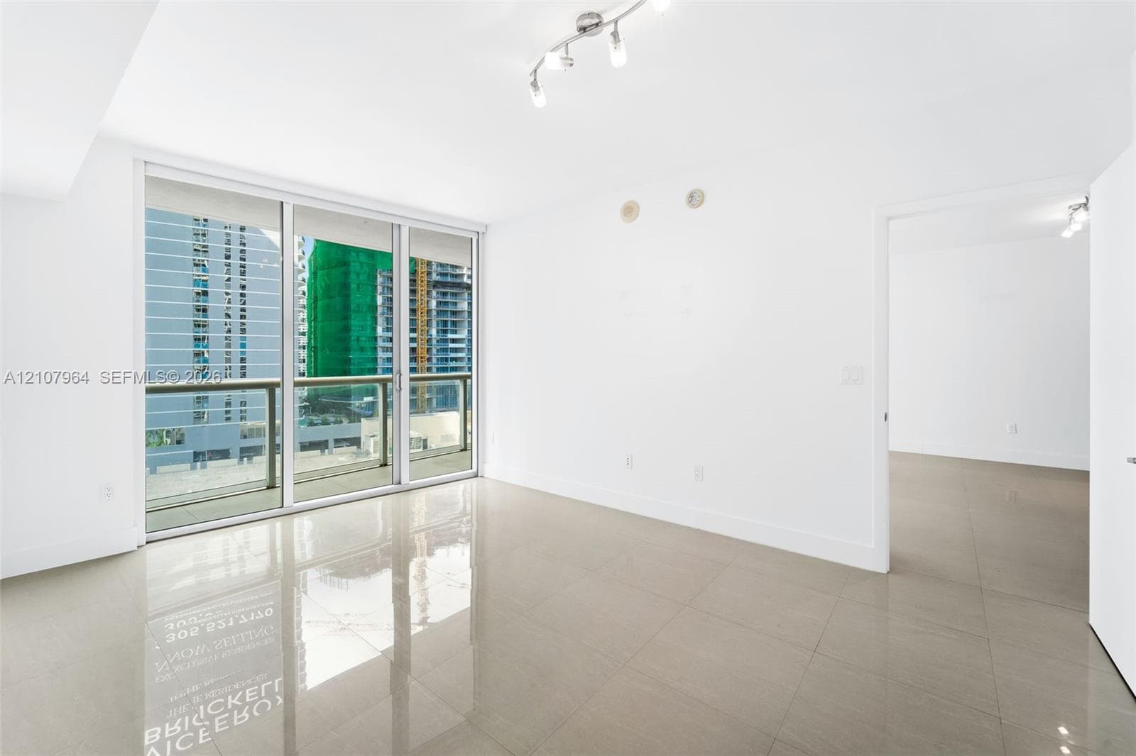 Large-format tile flooring, floor-to-ceiling glass sliding doors, covered balcony with metal railing, and multi-directional track lighting