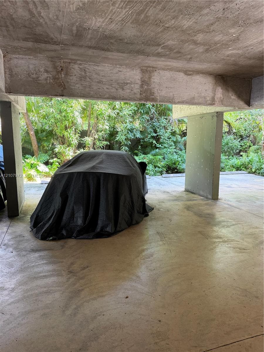 Covered parking area featuring concrete pillars, a textured concrete ceiling, and a concrete floor