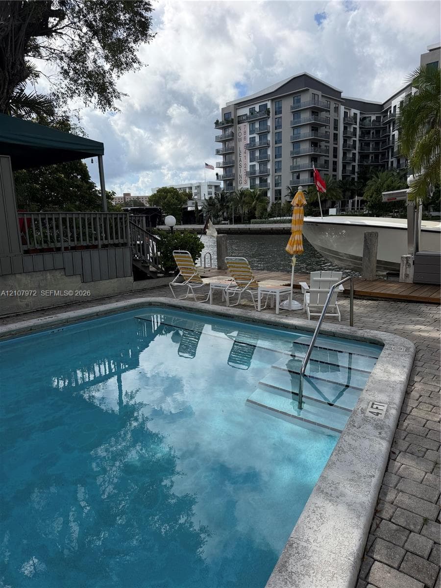 In-ground swimming pool with built-in stairs, concrete paver decking, and a private wooden dock situated on a waterway