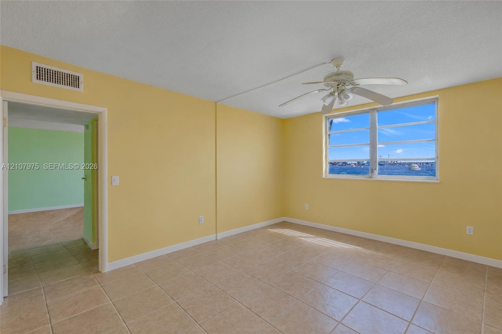 Waterfront multi-story residential building featuring screened-in balconies, concrete bulkhead, paved walkway, and manicured lawn