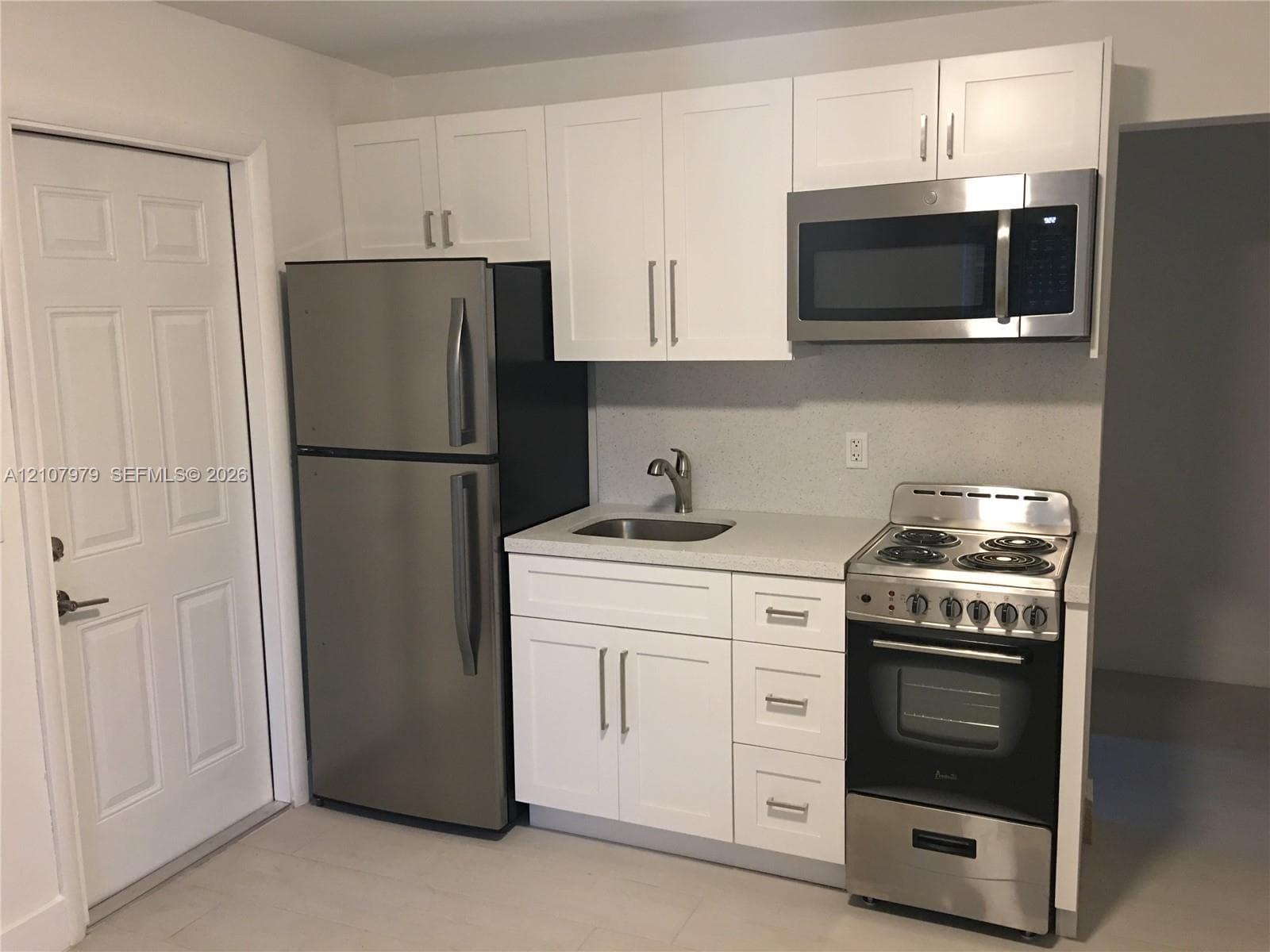 Kitchen area featuring white shaker-style cabinetry, solid-surface countertops, a stainless steel refrigerator, an over-the-range stainless steel microwave, and a stainless steel electric range