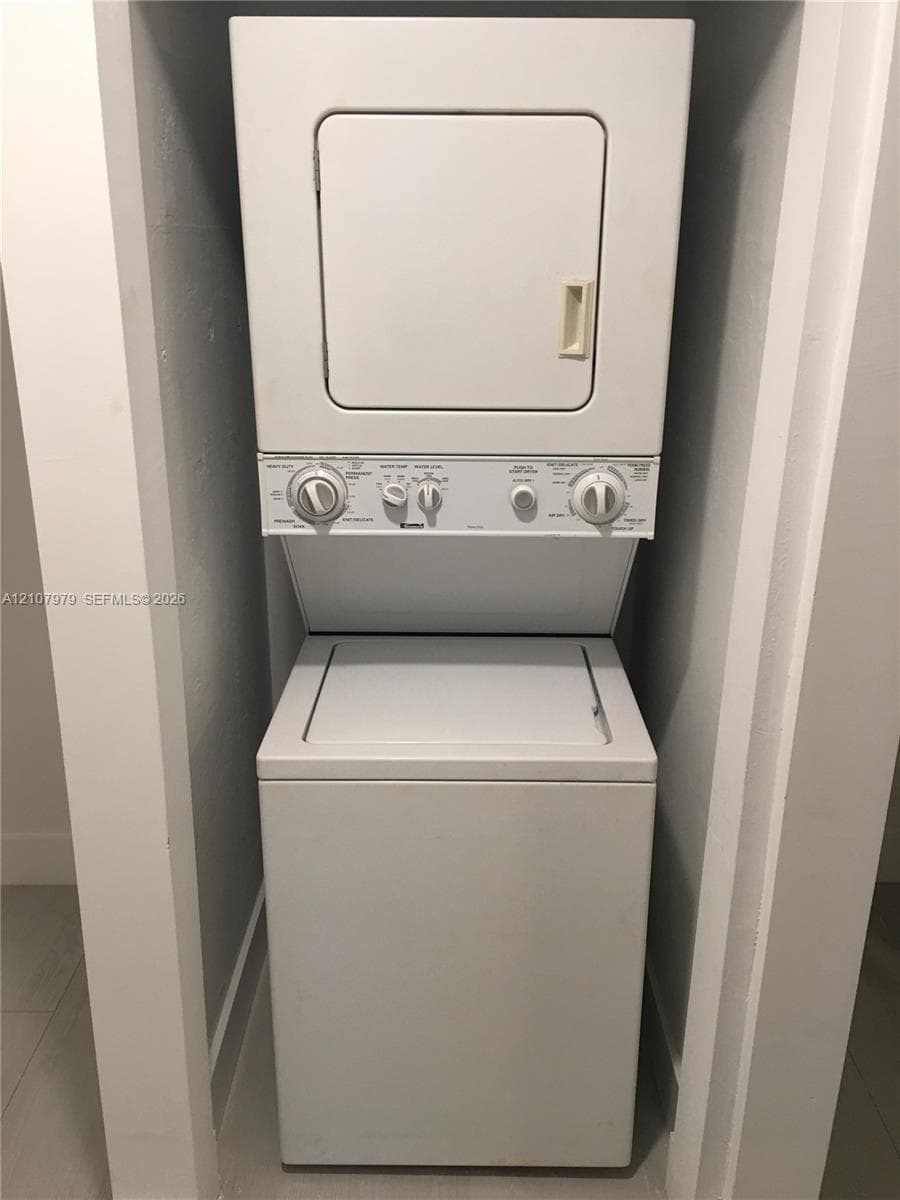 Stacked laundry unit featuring a white top-load washer and coordinating front-load dryer in a recessed closet space