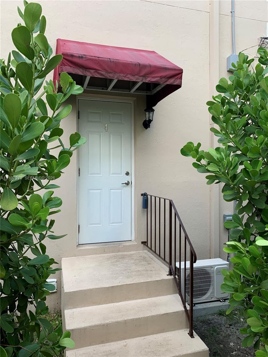 Exterior entry featuring a white six-panel door, metal awning, iron railing, and concrete steps