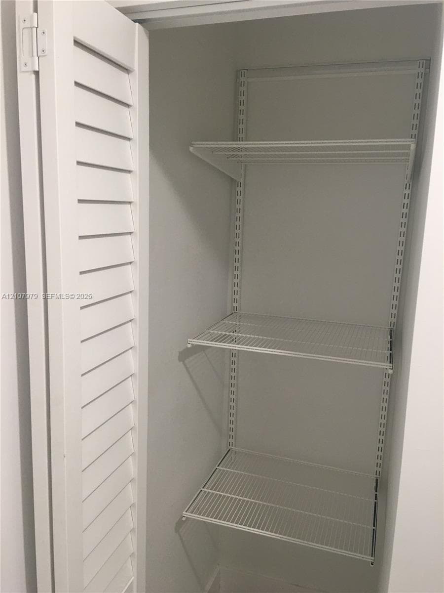 Storage closet featuring white louvered doors and adjustable wire shelving units