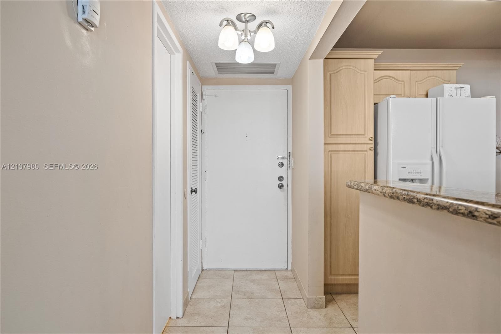 Entryway featuring tile flooring, a three-light semi-flush mount fixture, and built-in light-wood cabinetry with stone-finish countertops