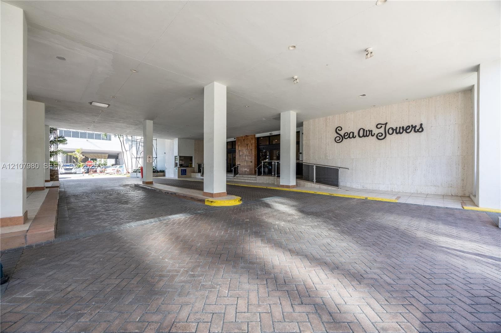 Covered porte-cochere entrance featuring a brick-paver driveway, structural support columns, and recessed ceiling lighting