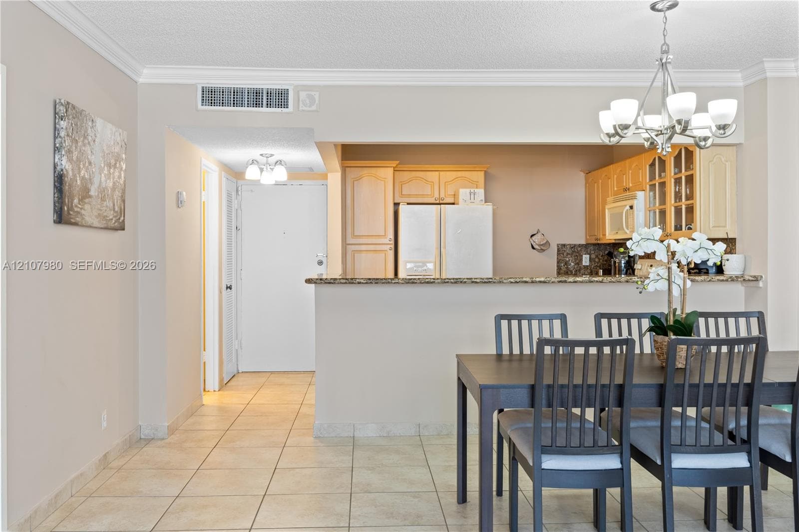 Kitchen featuring wood cabinetry, stone countertops, and a breakfast bar, complemented by tile flooring and a multi-light chandelier