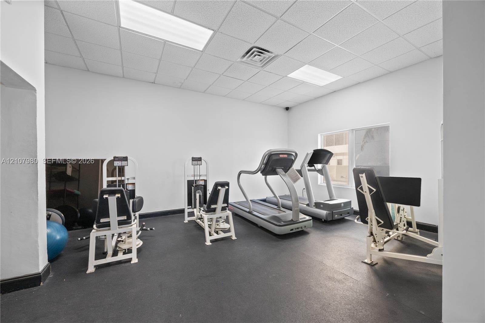 Fitness area featuring rubber flooring, recessed drop-ceiling tiles, and inset rectangular lighting