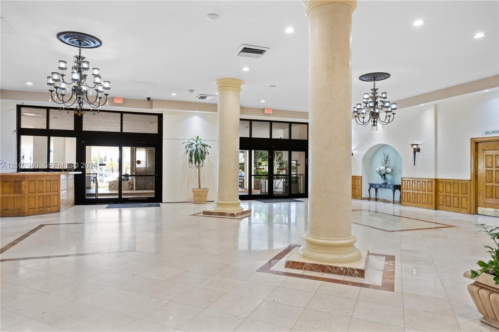 Grand foyer featuring tile flooring, structural columns, ornate chandeliers, recessed lighting, and wood-paneled accents