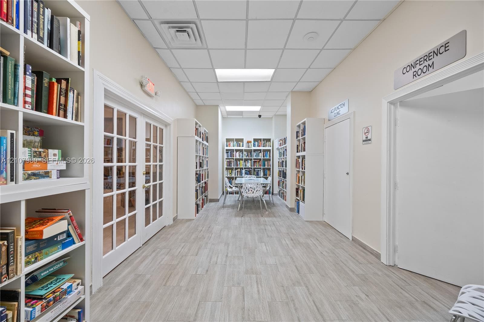Interior hallway featuring wood-finish flooring, drop ceiling with recessed lighting, and multiple floor-to-ceiling built-in white shelving units