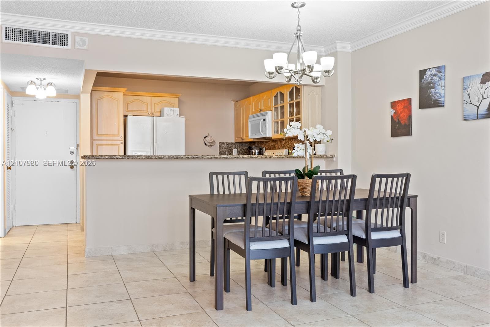 Dining area featuring ceramic tile flooring, crown molding, and a multi-light chandelier, complemented by a kitchen with built-in cabinetry and a stone-topped breakfast bar