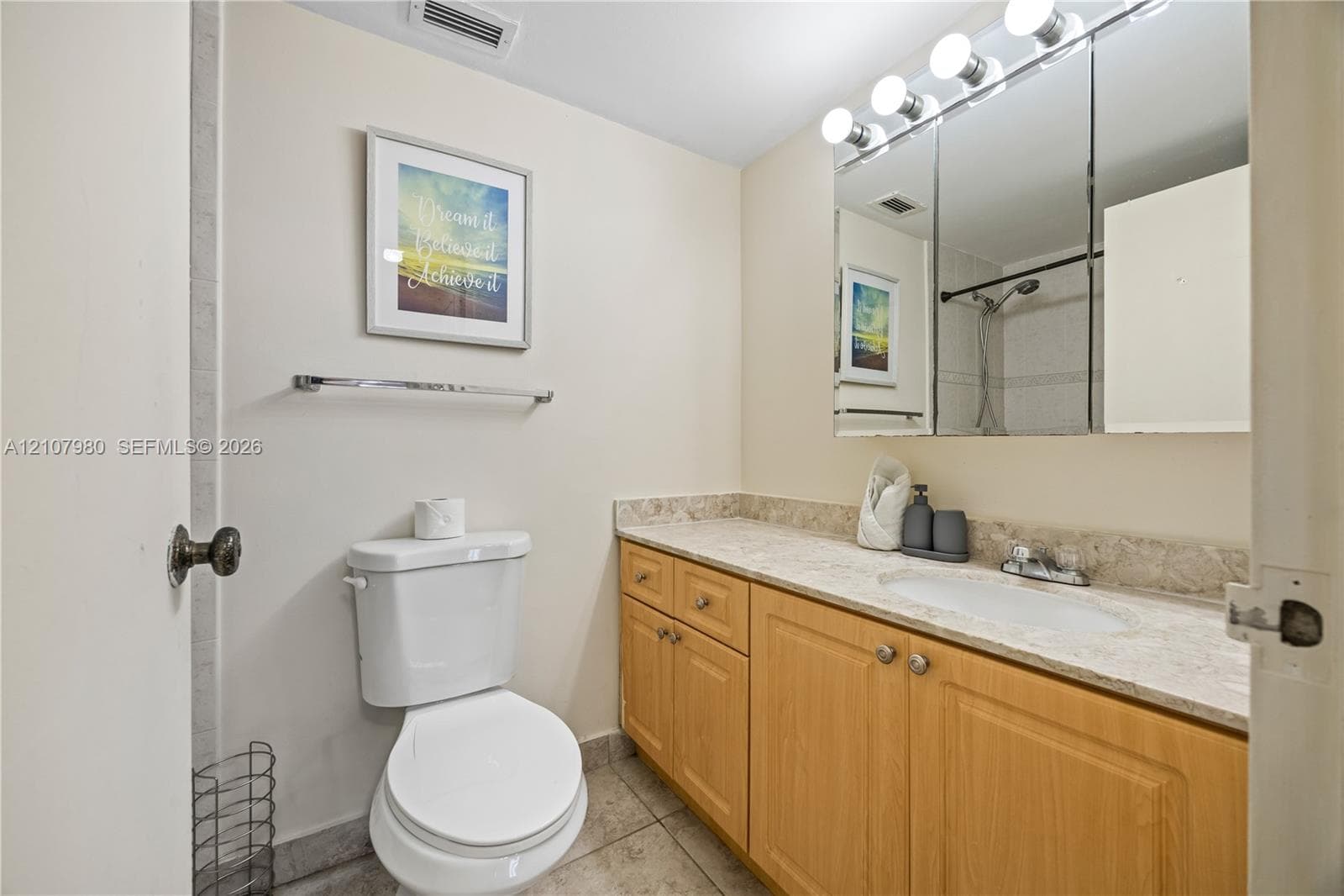 Full vanity with stone-finish countertop, integrated sink, three-door mirrored medicine cabinet, and wood-finish cabinetry