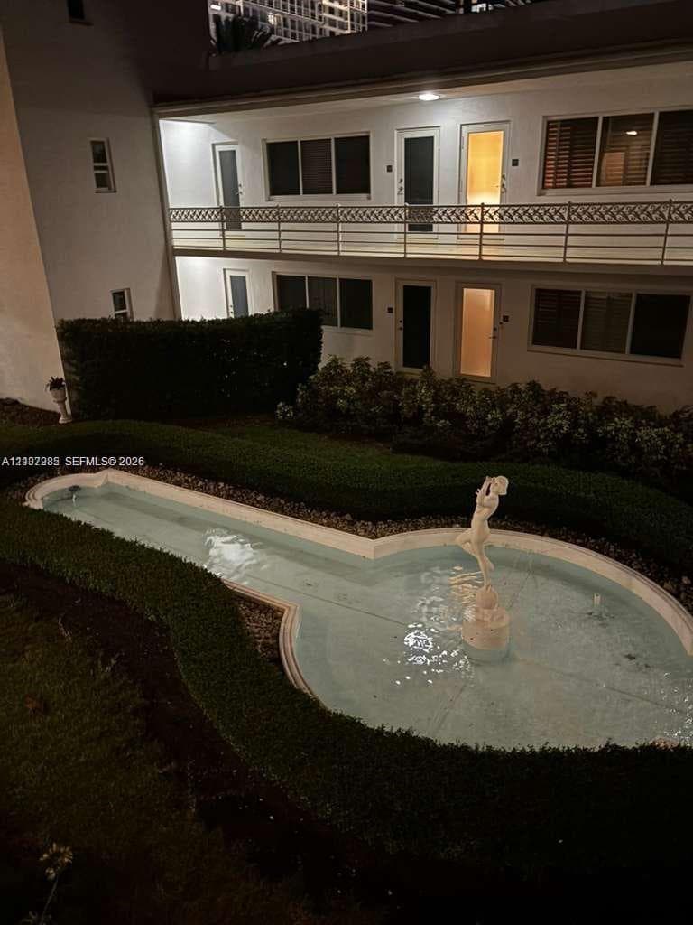Stucco exterior featuring a second-story balcony with metal railing, manicured landscaping, and a central sculptural fountain basin