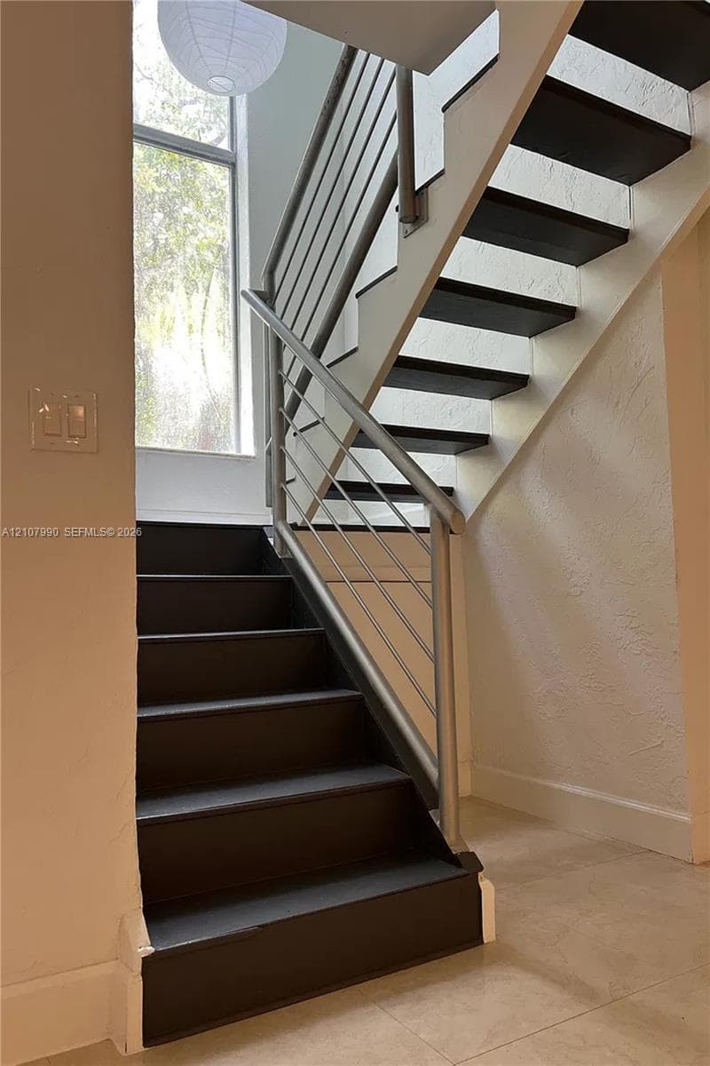 Staircase featuring dark wood-finish treads, metallic railings, a floor-to-ceiling window, and tile flooring