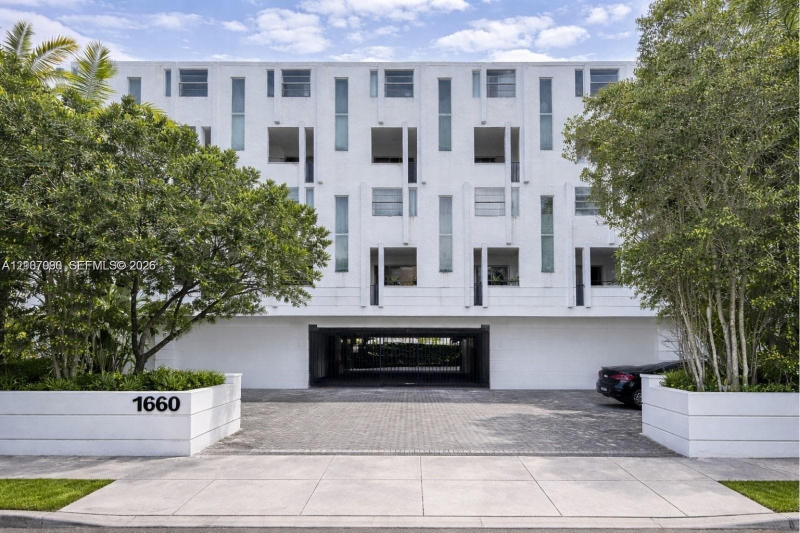Multi-story exterior with white masonry facade, integrated covered parking, vertical window arrangement, and concrete planters