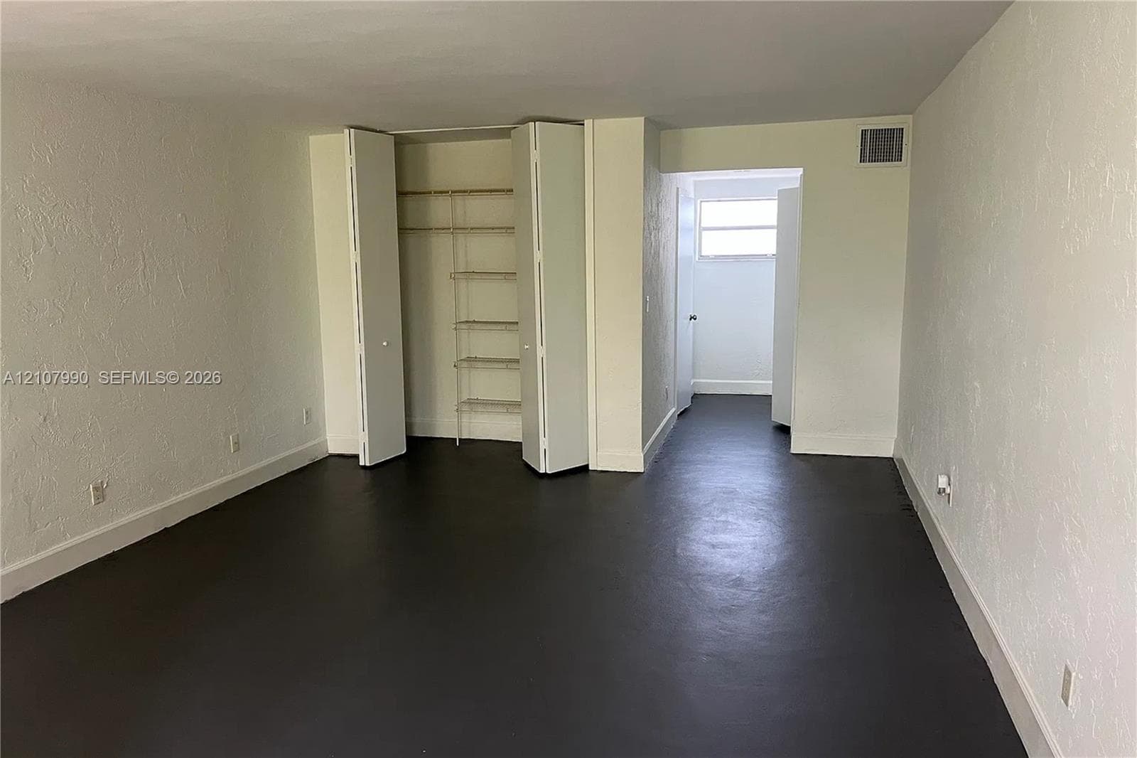 Interior space featuring dark flooring, textured wall finishes, and a built-in closet with integrated wire shelving