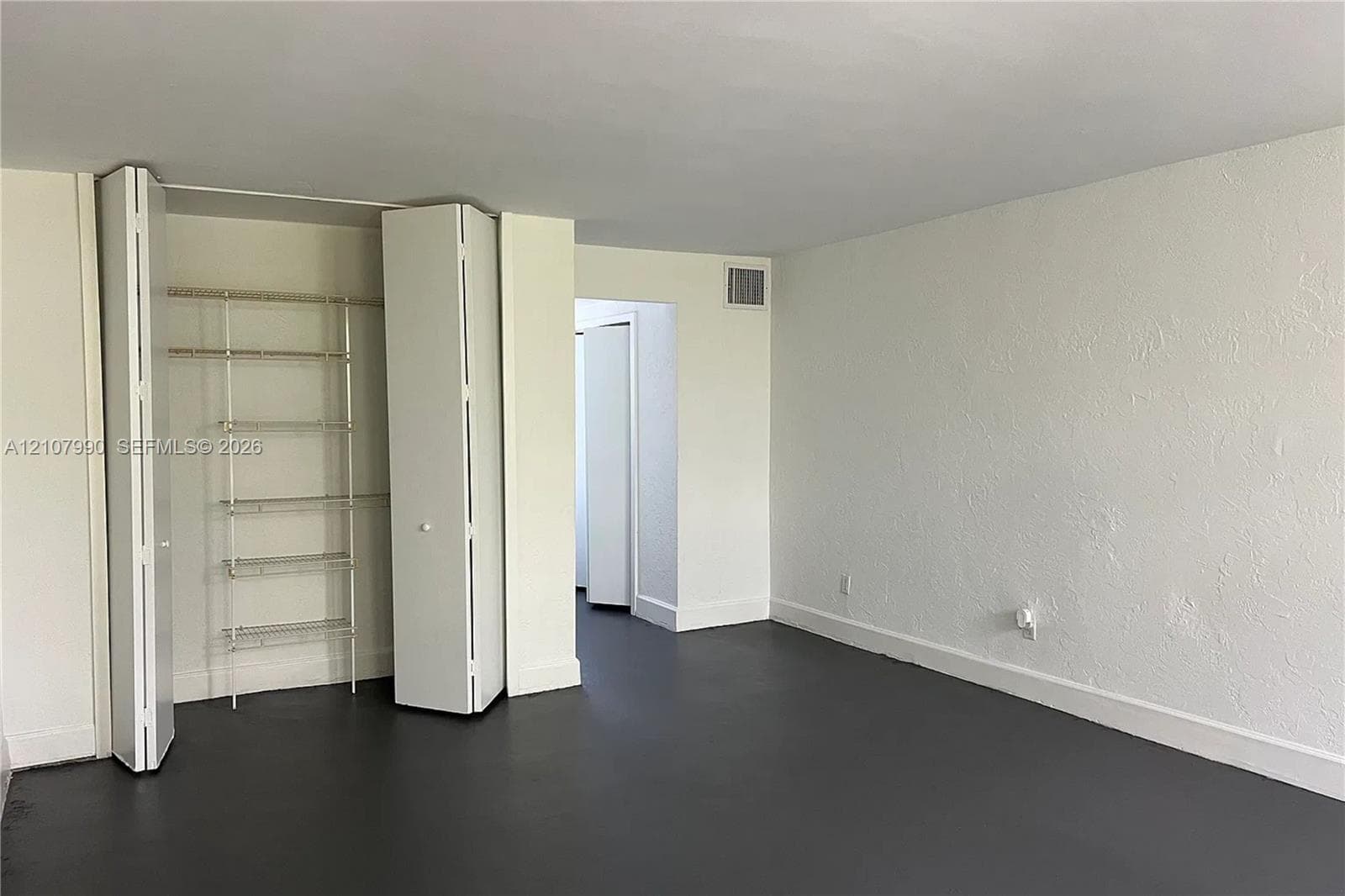 Interior space featuring crisp white walls, dark-toned flooring, and a walk-in closet with integrated wire shelving and bi-fold doors