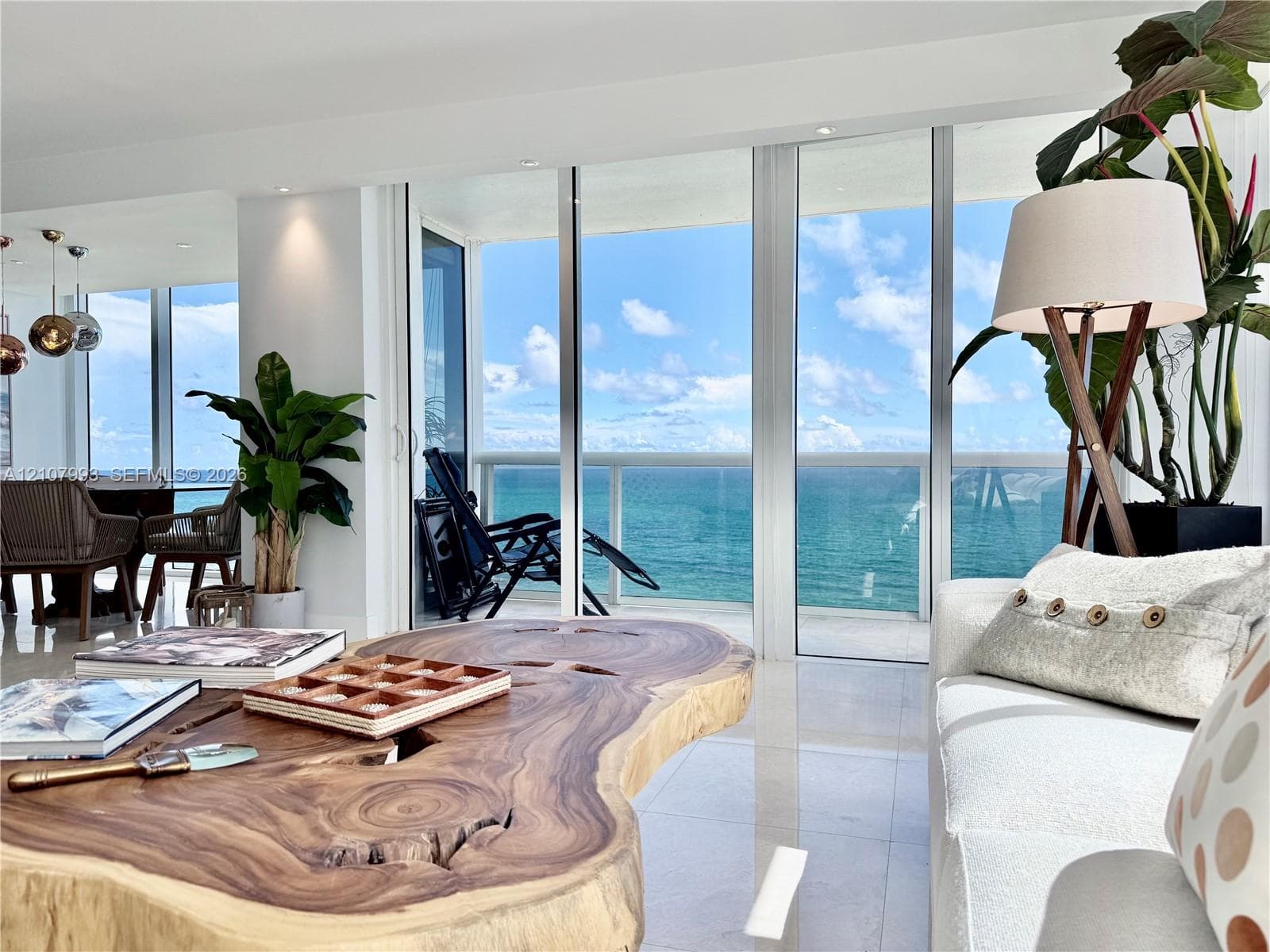 Floor-to-ceiling glass panel walls, light-reflective stone flooring, recessed ceiling lighting, and a glass-railed balcony overlooking the ocean