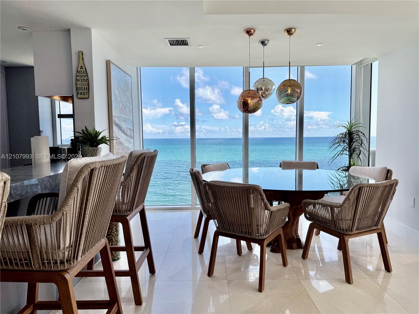 Floor-to-ceiling windows with ocean backdrop, polished stone flooring, and trio of spherical pendant light fixtures