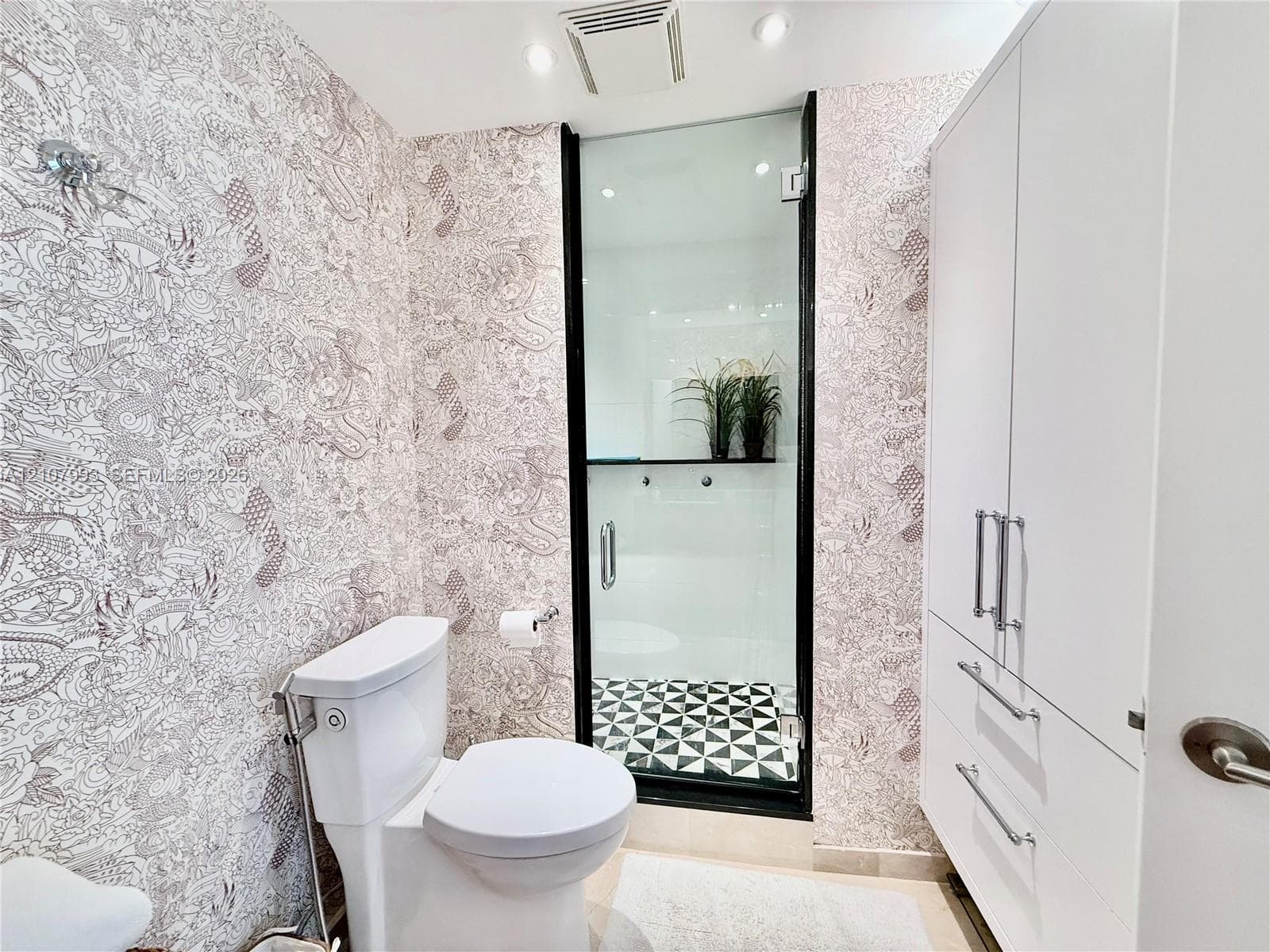 Bathroom featuring patterned wall coverings, a built-in white cabinetry unit with silver-tone hardware, a glass-enclosed shower with black trim, and geometric patterned flooring