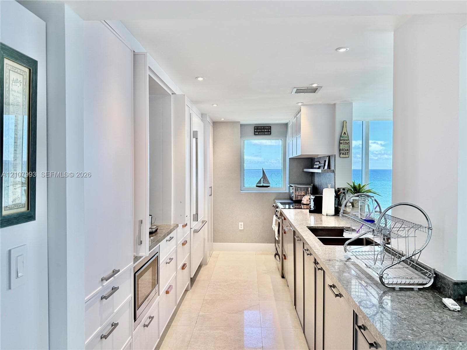 Kitchen featuring flat-panel white cabinetry, stone-surface countertops, recessed lighting, and large windows with ocean scenery