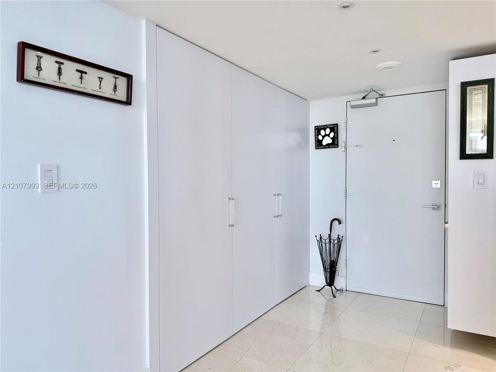 Floor-to-ceiling built-in white cabinetry with chrome hardware, polished stone tile flooring, and solid-core metal entry door with overhead hydraulic closer