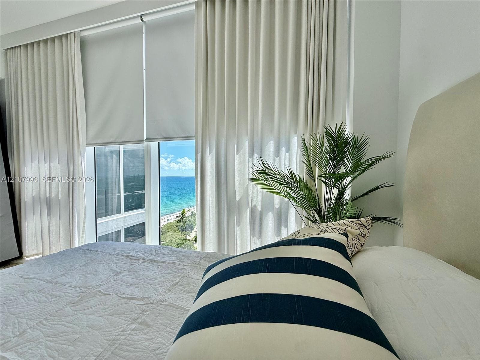 Floor-to-ceiling windows featuring automated roller shades and neutral drapery, providing a horizon of the ocean and coastal shoreline