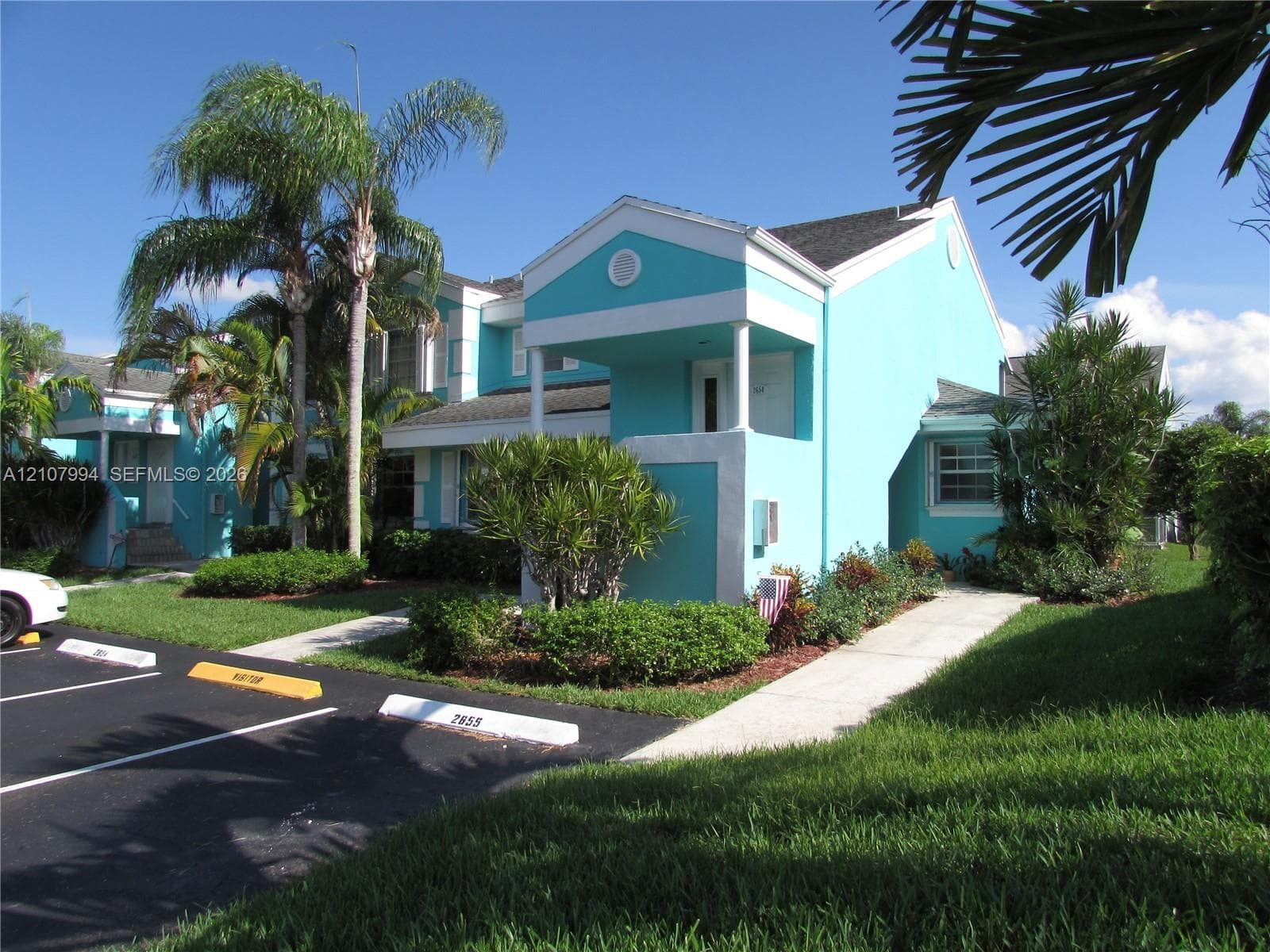 Exterior facade featuring a covered entryway, gabled roofline, concrete walkways, and mature palm landscaping