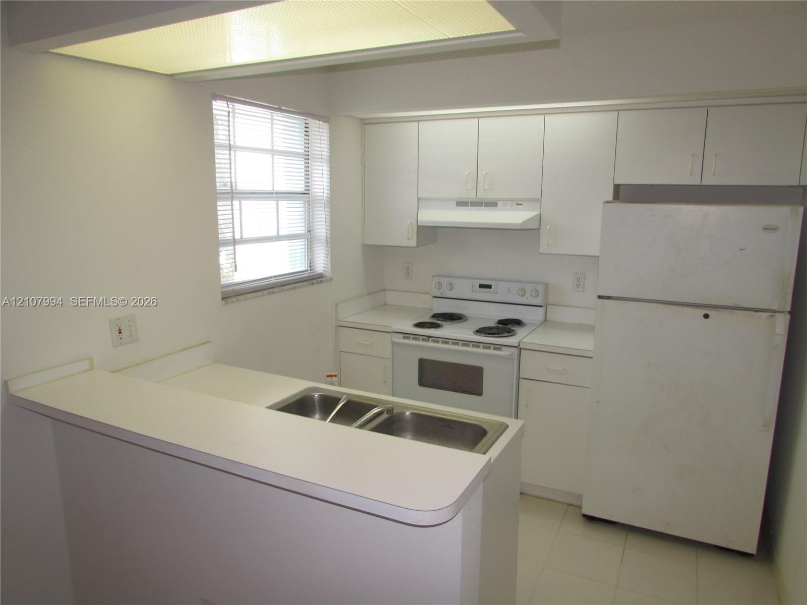 Kitchen featuring white cabinetry, solid-surface countertops, dual-basin stainless steel sink, electric range, and integrated fluorescent lighting